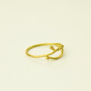 May include: A gold ring with a delicate, abstract design featuring a curved line and small, rounded accents.