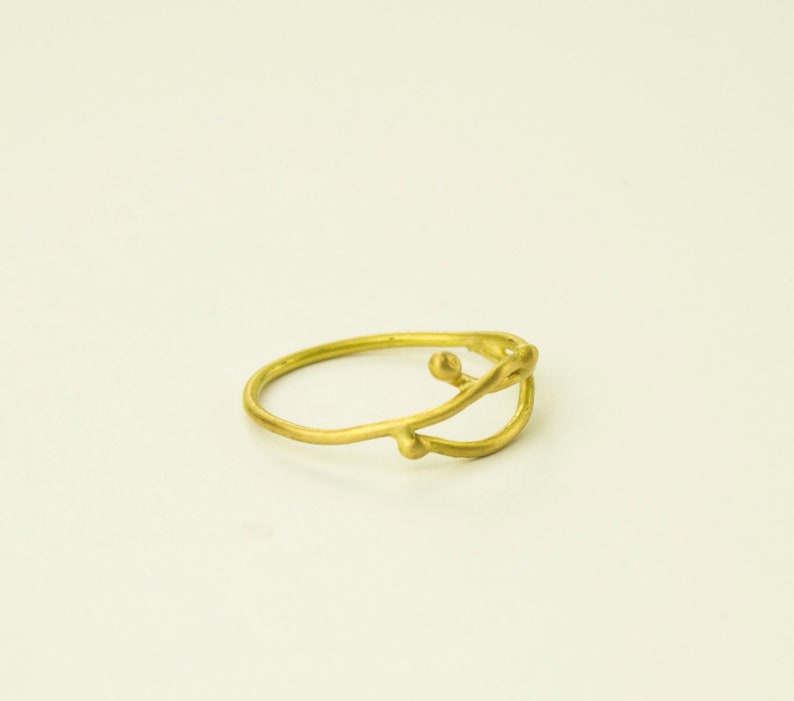 May include: A gold ring with a delicate, abstract design featuring a curved line and small, rounded accents.
