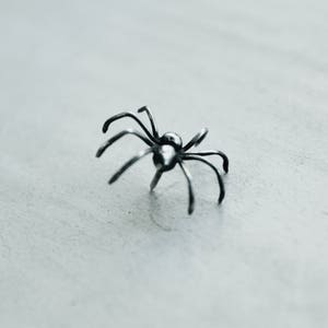 May include: A silver spider sculpture with a detailed design. The spider is posed with its legs outstretched.