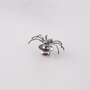 May include: A silver spider brooch with eight legs and a round base.