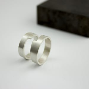 Puede incluir: Dos anillos de plata con un diseño único. Los anillos están apilados uno encima del otro y tienen un espacio en el medio.