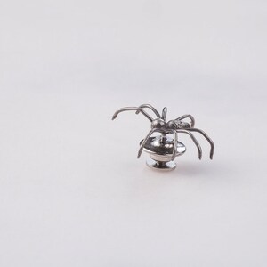 May include: Silver spider brooch with a round base. The spider has eight legs and is in a crawling position.