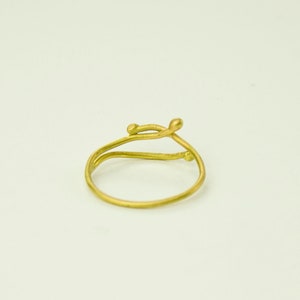 May include: A gold ring with a delicate, twisted design. The ring is made of a single piece of wire that is twisted and shaped to create a unique and modern look.