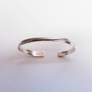 May include: A silver bangle bracelet with a textured band.