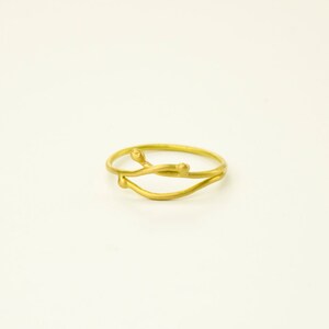 May include: A gold ring with a delicate, twisted design. The ring features two thin bands that intertwine and have small, rounded accents.