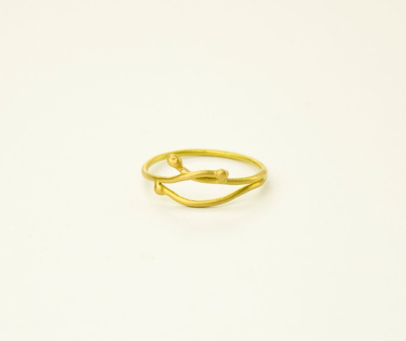 May include: A gold ring with a delicate, twisted design. The ring features two thin bands that intertwine and have small, rounded accents.