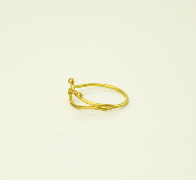 May include: A gold ring with a delicate, organic design. The ring features two intertwined bands with small, rounded accents.