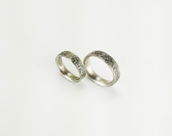 May include: Two silver wedding bands with a textured finish.