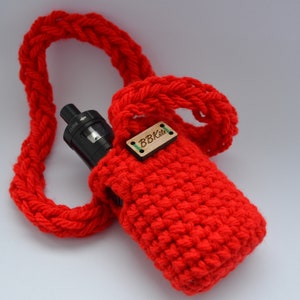 May include: A bright red, crocheted vape case with a matching strap. The case holds a black vape device. A small wooden tag with the text "BBKits" is attached to the case.