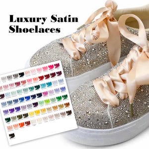 May include: A pair of silver rhinestone sneakers with peach satin ribbon laces. The sneakers have white soles and a variety of satin shoelace color options are displayed on a card.