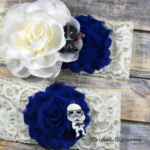 May include: Two white lace garters with blue and white fabric flowers. One garter features a black Darth Vader charm and the other features a white Stormtrooper charm. The text "Bridal Blossoms" is visible in the bottom right corner of the image.