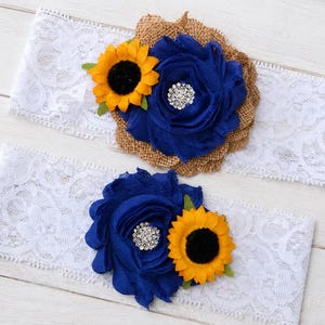 May include: Two white lace bands featuring decorative floral arrangements. Each band includes a large blue fabric flower with a central rhinestone embellishment, a smaller yellow sunflower, and a textured brown burlap backing element.