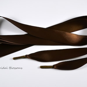 May include: A brown satin ribbon with two metal ends. The ribbon is approximately 1.5 inches wide and is tied in a knot.