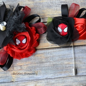 May include: Two red and black fabric flower brooches with a Spider-Man character button in the centre. The larger brooch has a black bow and a pearl-like bead. The smaller brooch is on a pin.