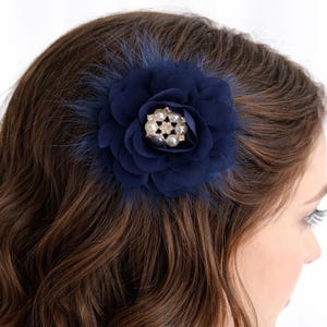 May include: A navy blue fabric flower hair accessory featuring layered petals, dark blue feathers, and a central embellishment composed of small white faux pearls and clear crystals arranged in a circular pattern on a metal base.
