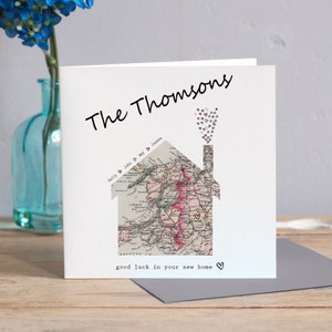 May include: A square white card featuring a house-shaped map design. The card says "The Thomsons" and "good luck in your new home." The house is filled with a vintage map, and hearts are used as decorative elements.