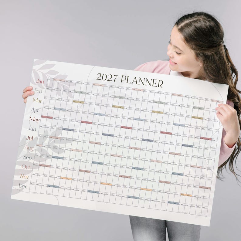 May include: A large wall calendar titled 2027 PLANNER with a white background and a grid layout. The months from January to December are listed on the left side in black text. The design features subtle gray leaf illustrations on the left side.