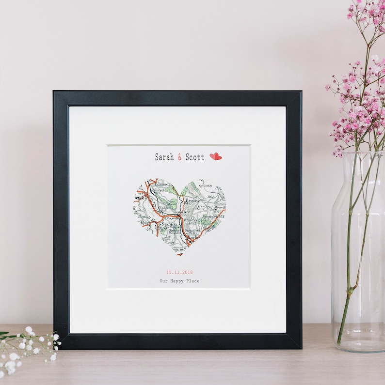 May include: A black framed print with a white background. The print features a map of a region in the shape of a heart with the text "Sarah & Scott" and "15.11.2018 Our Happy Place" below the map.