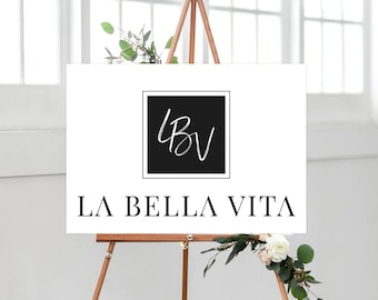 May include: A white sign with black lettering and a black square with white lettering that says "LBV" in cursive. The sign says "LA BELLA VITA" and is on an easel.
