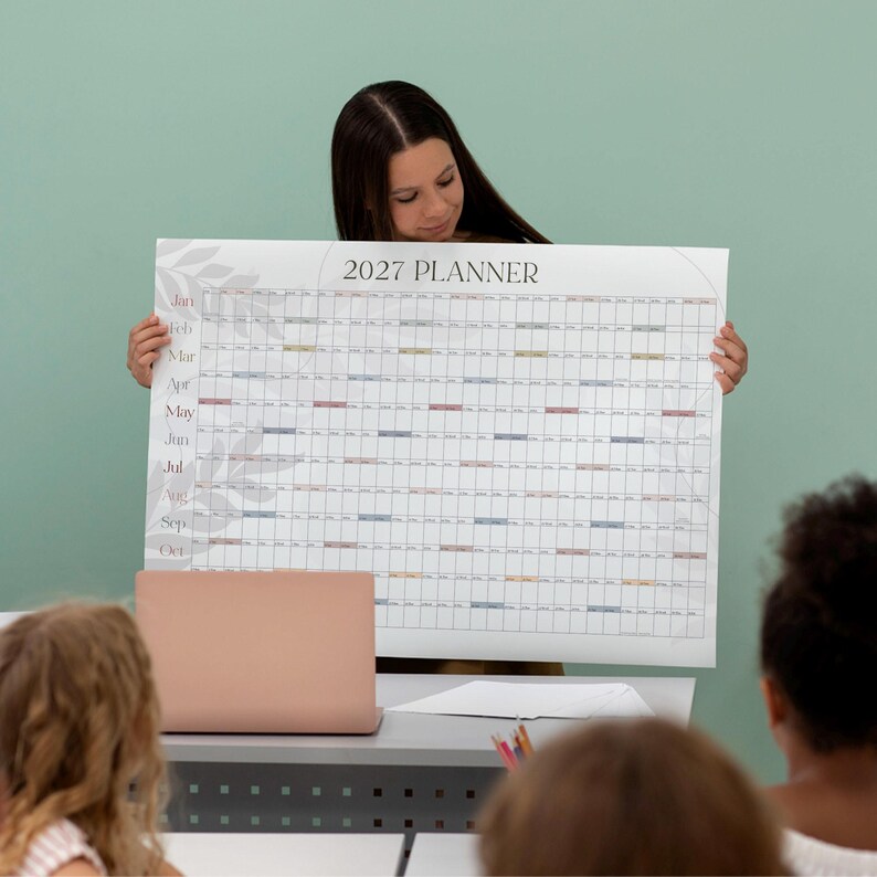 May include: A large horizontal 2027 wall planner calendar featuring a grid layout with months listed vertically on the left side. The design includes subtle gray leaf illustrations on the left border and small colored rectangular accents.