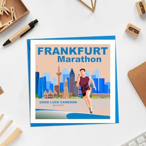 May include: A blue and orange card with the text "FRANKFURT Marathon" and a graphic of a runner in front of a city skyline. The text "GOOD LUCK CAMERON 08.10.2023" is at the bottom of the card.