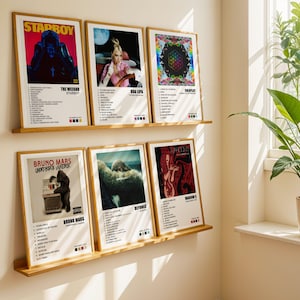 May include: Six framed posters on a wall, each featuring a different album cover. The posters are arranged in two rows of three. The top row features posters for The Weeknd's "Starboy", Dua Lipa's self-titled album, and Coldplay's "A Head Full of Dreams". The bottom row features posters for Bruno Mars' "Unorthodox Jukebox", Beyonce's "Beyonce", and Madonna's "Confessions on a Dance Floor".