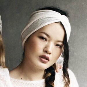 May include: A white and gray knit turban headband with a knotted design. The headband is worn by a person with long black hair.