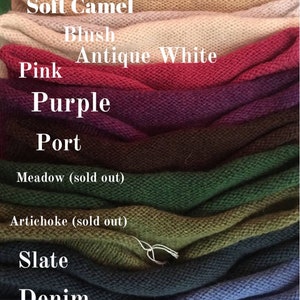 May include: A stack of knitted fabric swatches in various colors, including peach, otter, soft camel, blush, antique white, pink, purple, port, meadow, artichoke, slate, denim, and duck egg green. The swatches are labeled with their corresponding color names.