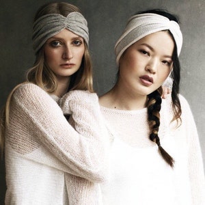 May include: Two women wearing white knit sweaters and gray headbands. One woman has long blonde hair and the other has long black hair with a braid.