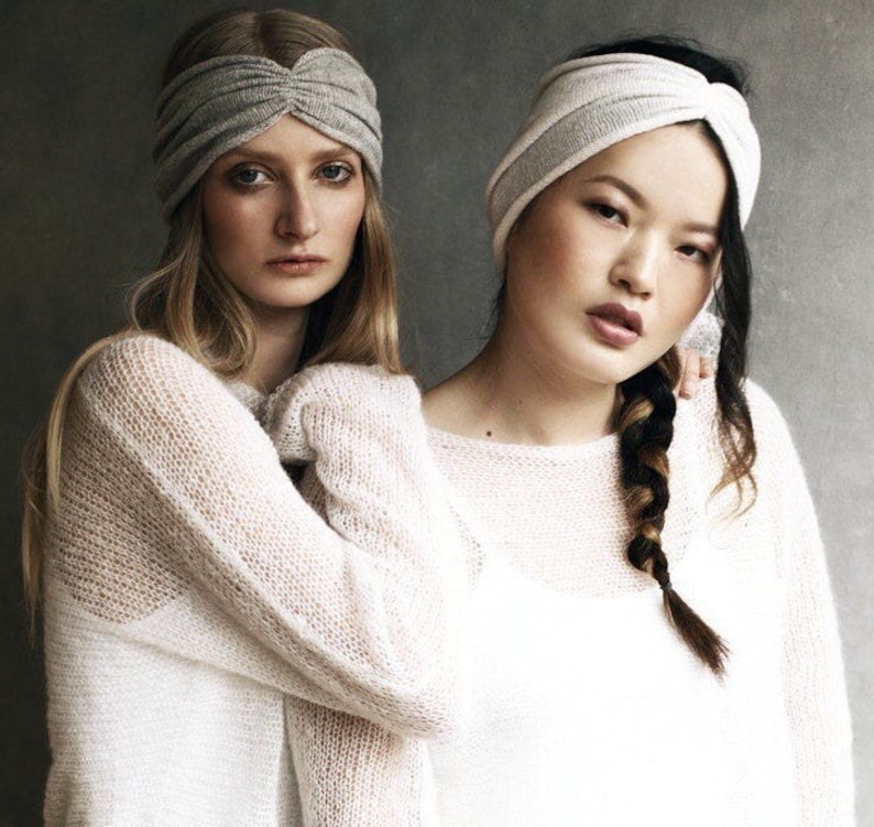 May include: Two women wearing white knit sweaters and gray headbands. One woman has long blonde hair and the other has long black hair with a braid.