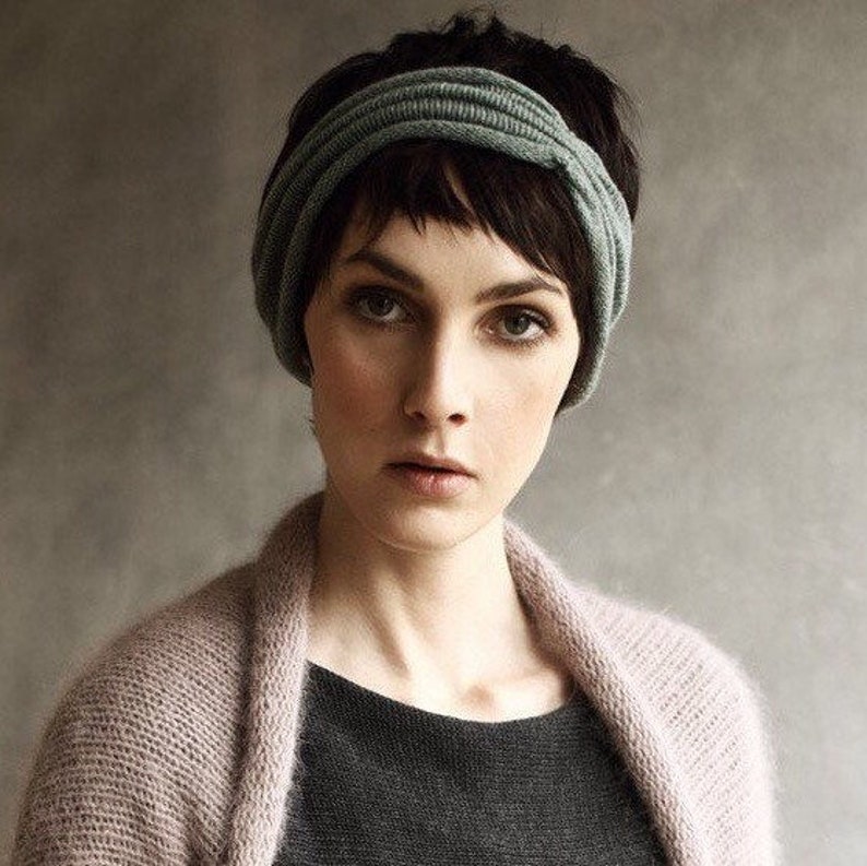 May include: A woman with short, dark hair is wearing a light pink cardigan and a gray headband. She is looking at the camera.