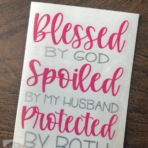 Puede incluir: Un fondo blanco con el texto "blessed by god spoiled by my husband protected by both" en letras rosas y grises.