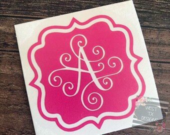 May include: A pink vinyl decal with a white outline featuring a stylized letter A with swirls. The decal is on a white background.