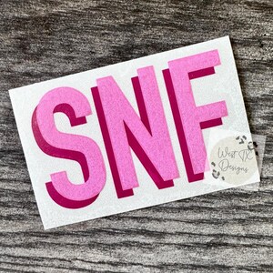 May include: A rectangular sticker featuring the letters SNF in a bold, sans-serif font. The letters are light pink with a dark magenta drop shadow. A small circular logo with a leopard print border and the text West TX Designs is in the corner.