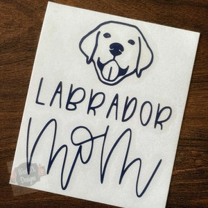 Pu&ograve; includere: Adesivo in vinile bianco con un contorno blu di una testa di cane Labrador Retriever e il testo "Labrador Mom" in un font corsivo.
