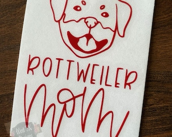 May include: A white rectangle with a red Rottweiler dog illustration and the words "ROTTWEILER MOM" in red script. The dog illustration is a simplified outline of a Rottweiler's head with a smiling expression.