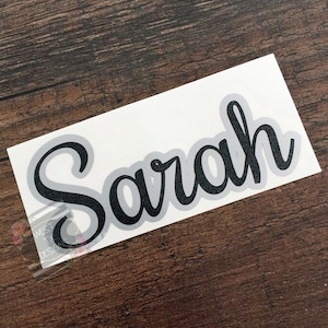 May include: A white vinyl sticker with the name "Sarah" written in black cursive script.