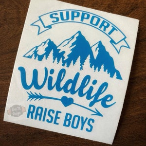 May include: Blue vinyl decal with the text "Support Wildlife Raise Boys" with a mountain range and arrow graphic.