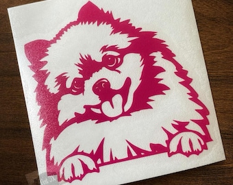 Könnte beinhalten: Ein magentafarbener Vinyl-Aufkleber mit einer stilisierten Illustration eines flauschigen Hundes mit spitzen Ohren, einem weit aufgerissenen Blick und offenem Maul, bei dem die Zunge zu sehen ist. Der Hund schaut über eine horizontale Kante.