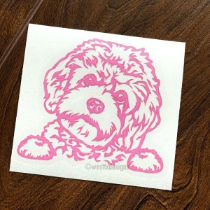 May include: Pink vinyl decal of a dog's head with a fluffy, curly hairstyle. The dog is looking directly at the viewer with its mouth closed. The decal is on a white background. ©westbxdesigns