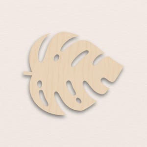 Könnte beinhalten: Holzausschnitt in Form eines Monstera-Blattes in hellem Braun. Das Blatt hat mehrere große, unregelmäßige Löcher und eine detaillierte Aderstruktur. Geeignet für Heimdekoration oder Bastelprojekte.