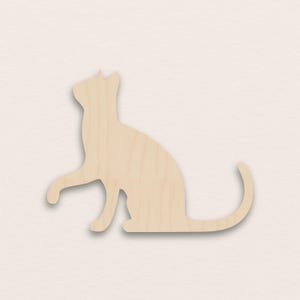 Puede incluir: Silueta de gato de madera en posición sentada con una pata levantada. El gato es de madera clara, con vetas visibles. La cola del gato está curvada y las orejas puntiagudas.