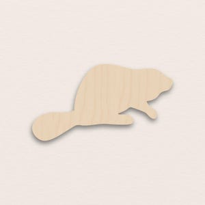 May include: A wooden beaver cutout, featuring a light brown color and a smooth finish. The beaver is depicted in a side profile, with its distinctive flat tail and a slightly raised paw. The cutout is ideal for crafts and DIY projects.