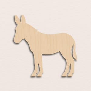 May include: A wooden donkey cutout in a standing profile. The donkey is light brown with visible wood grain. The cutout has a shadow effect, giving it a three-dimensional appearance. The donkey has long ears and a short tail.