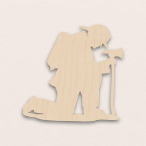 May include: A wooden cutout of a kneeling firefighter holding an axe. The figure is in a light brown color, with details of the firefighter's uniform and equipment. The axe is held upright, and the firefighter is kneeling on one knee.