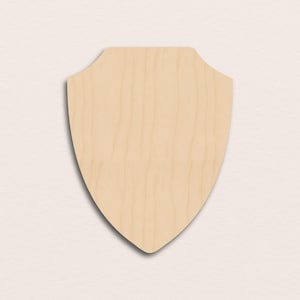 May include: A light-colored, unfinished wooden shield plaque with a rounded top and pointed bottom. The wood grain is visible, and the plaque is designed for mounting or display. The shield shape is a classic design, suitable for various craft projects.