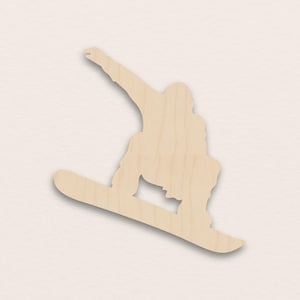 May include: A wooden cutout of a snowboarder in mid-air, with one arm extended. The figure is light brown, with a smooth, unpainted surface. The snowboarder is angled diagonally, suggesting motion and speed.