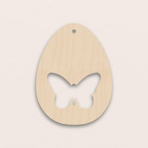 Pode incluir: Um ornamento de madeira clara em forma de ovo com um recorte de borboleta. O ornamento tem um pequeno orifício na parte superior para pendurar. O desenho da borboleta está centrado na forma do ovo.
