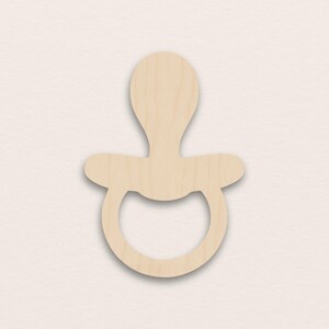 Puede incluir: Recorte de madera de un chupete en un tono de madera natural. El chupete tiene una tetina redondeada, un escudo y un anillo. El recorte está diseñado para manualidades o proyectos con temática de bebés.