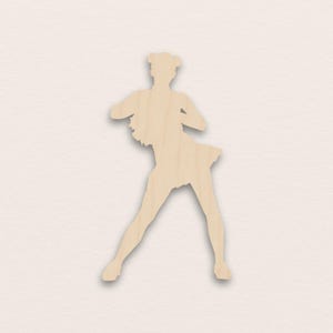 Könnte beinhalten: Hellbraune Holzaussparung in Form einer Balletttänzerin. Die Figur hat einen Rock und ausgestreckte Arme. Das Haar der Tänzerin ist zu zwei Duttfrisuren gestylt.